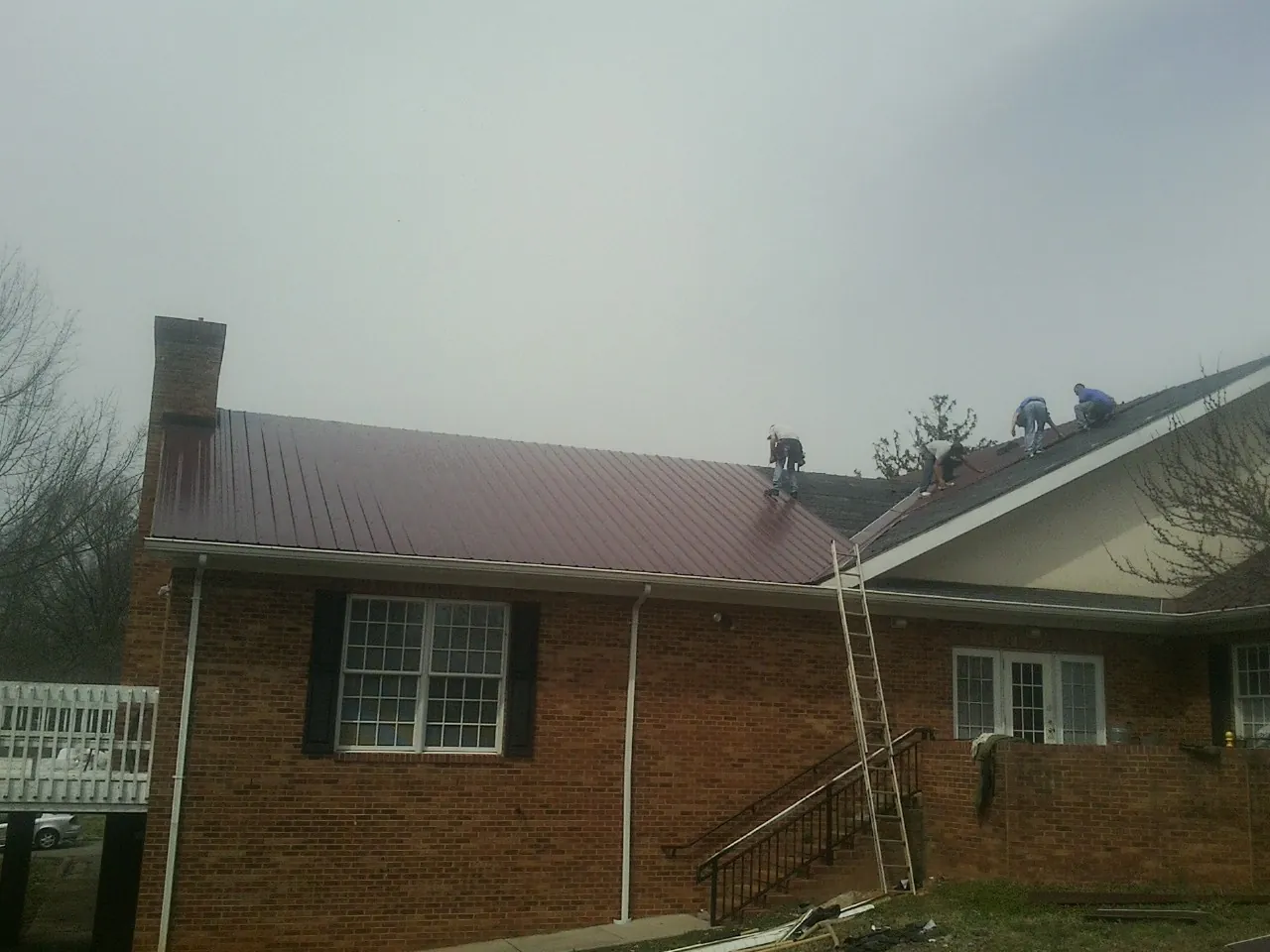 Crew setting red metal roofing panels on a brick home in Sheridan